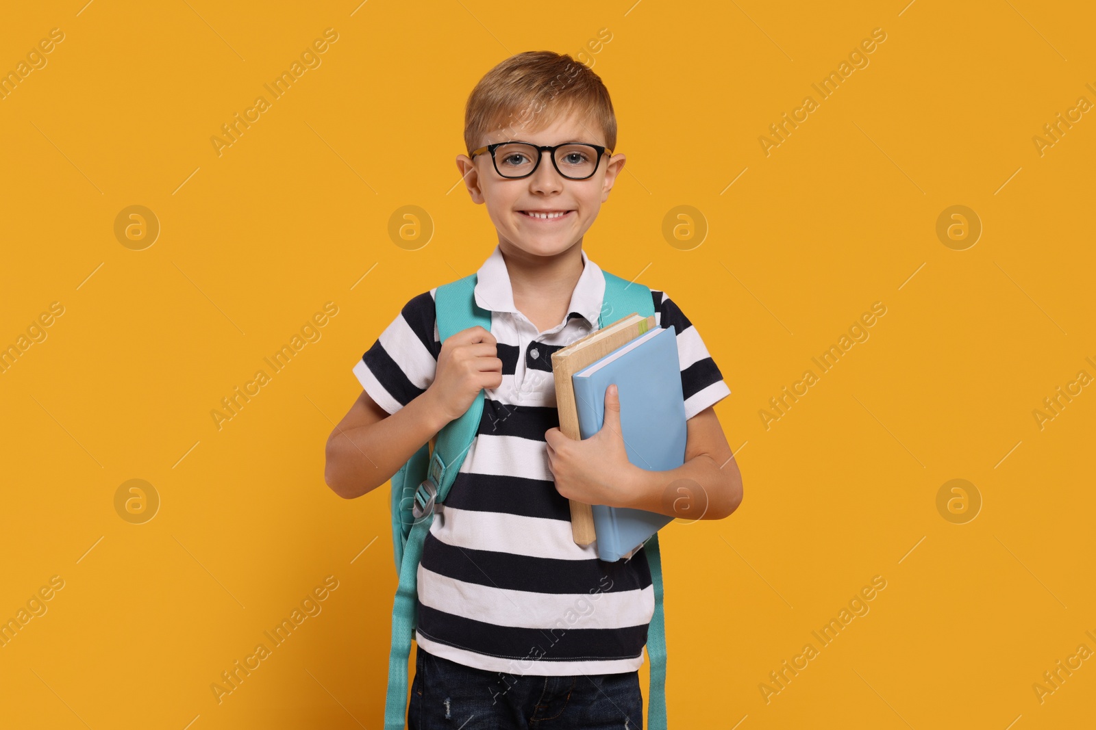 Photo of Happy schoolboy in glasses with backpack and books on orange background