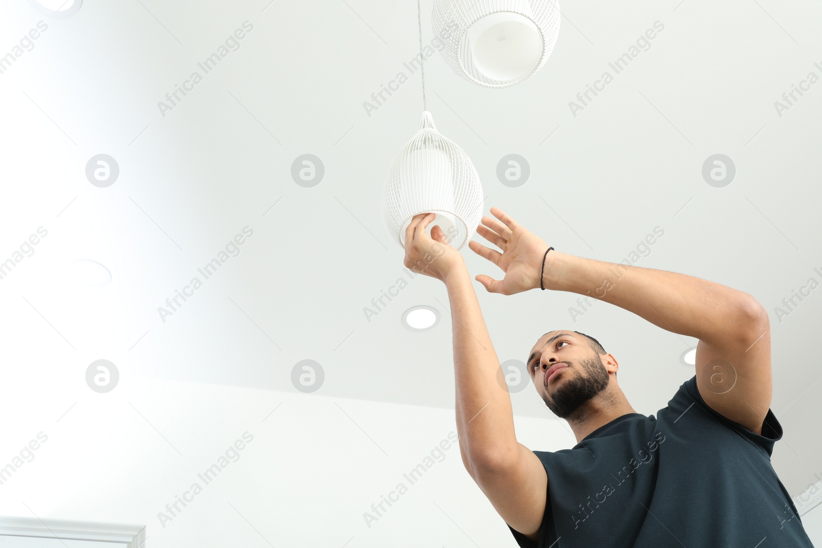 Photo of Young man repairing ceiling lamp indoors, low angle view. Space for text