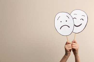 Woman with sad and happy paper faces on beige background, closeup. Space for text