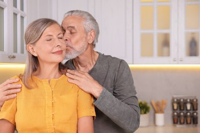 Senior man kissing his beloved woman in kitchen, space for text