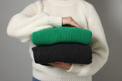 Woman with stack of knitted sweaters on grey background, closeup