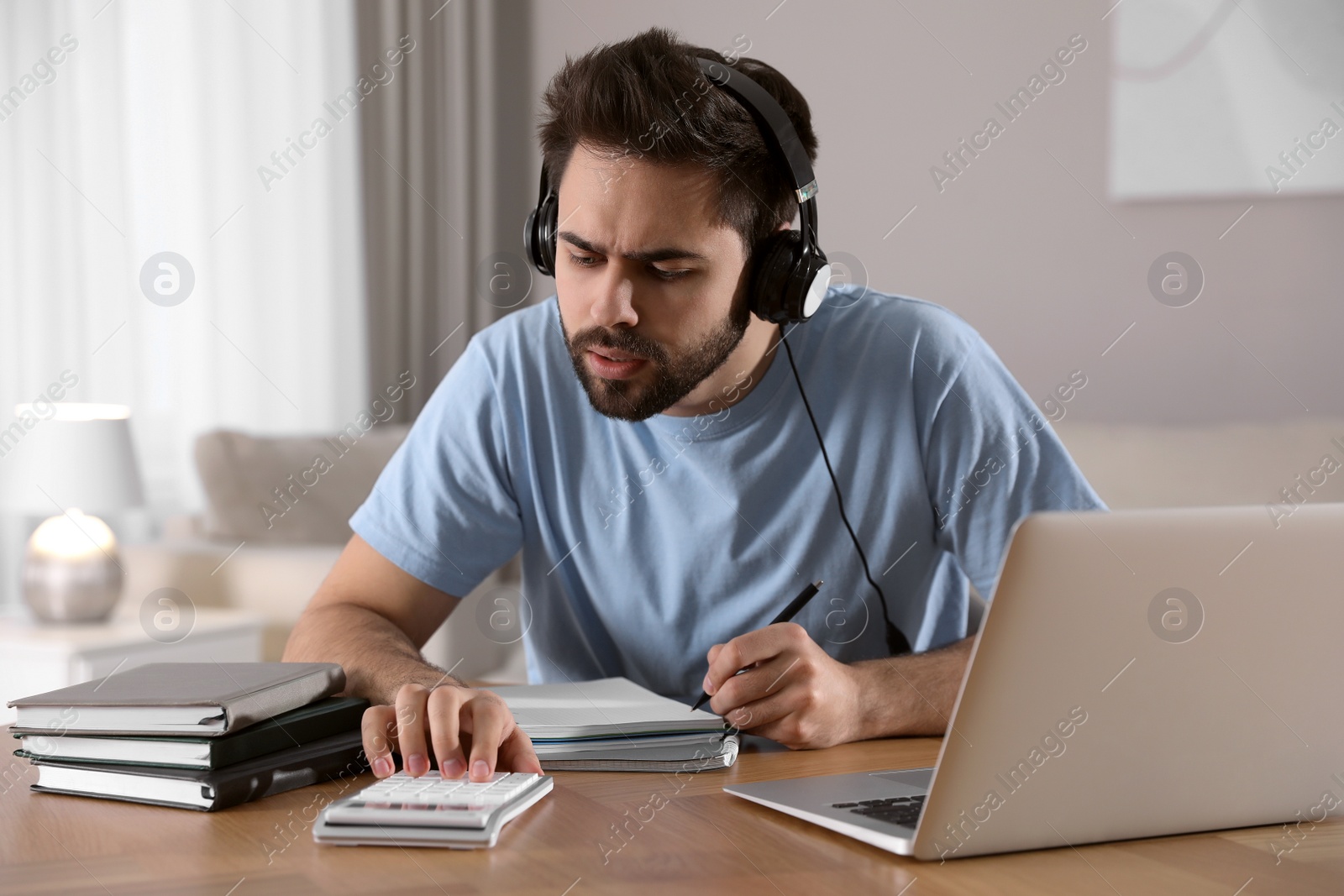 Photo of Young man counting on calculator during webinar at table in room