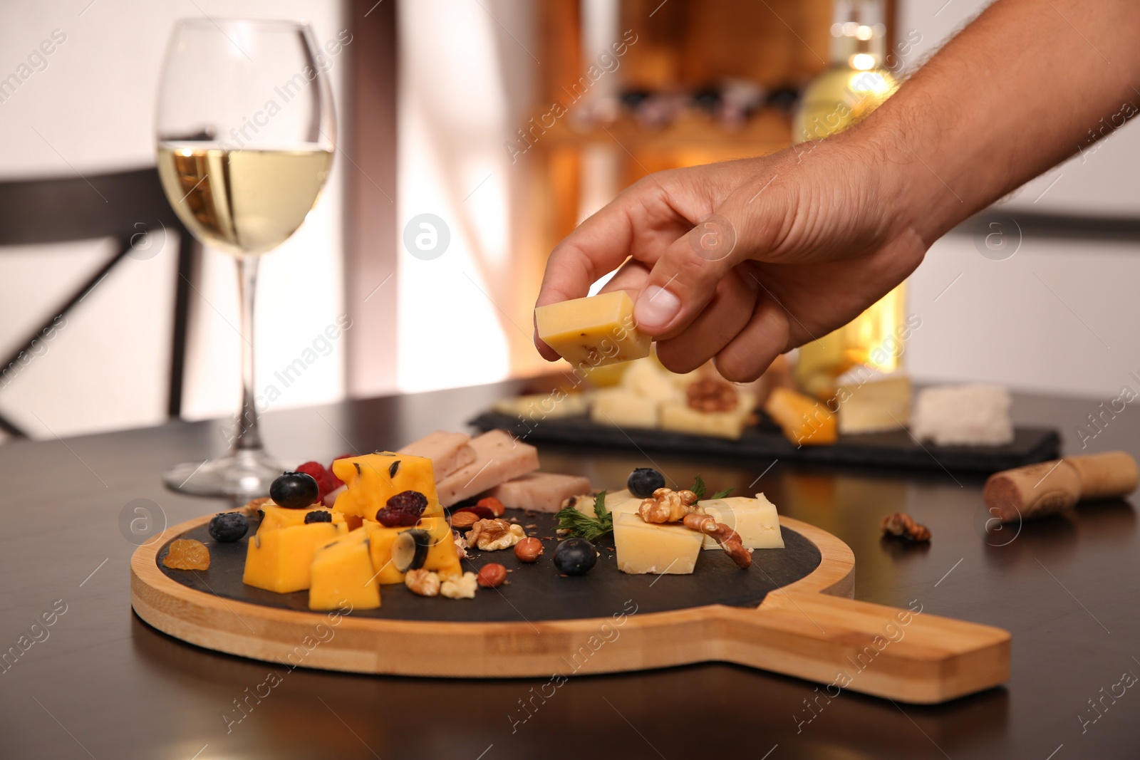 Photo of Man taking piece of delicious cheese at table indoors, closeup