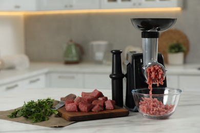 Electric meat grinder with beef mince and parsley on white table in kitchen