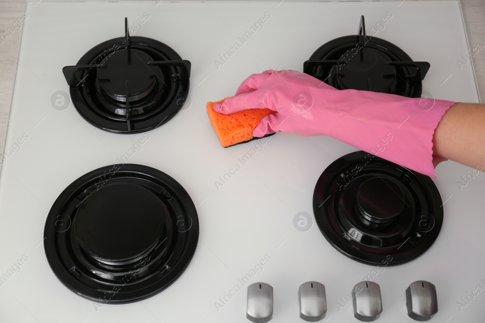 Photo of Woman cleaning gas stove with sponge, closeup