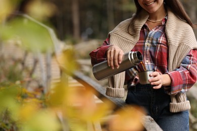 Photo of Woman pouring hot drink from metallic thermos into cup lid outdoors, closeup. Space for text