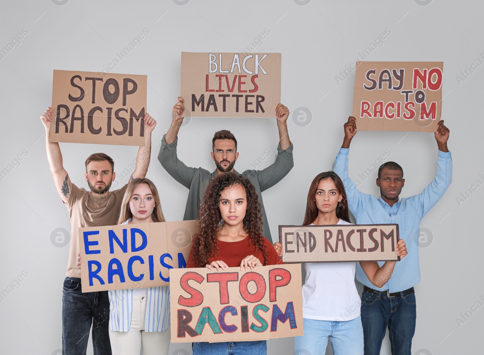 Photo of Protesters demonstrating different anti racism slogans on light background. People holding signs with phrases