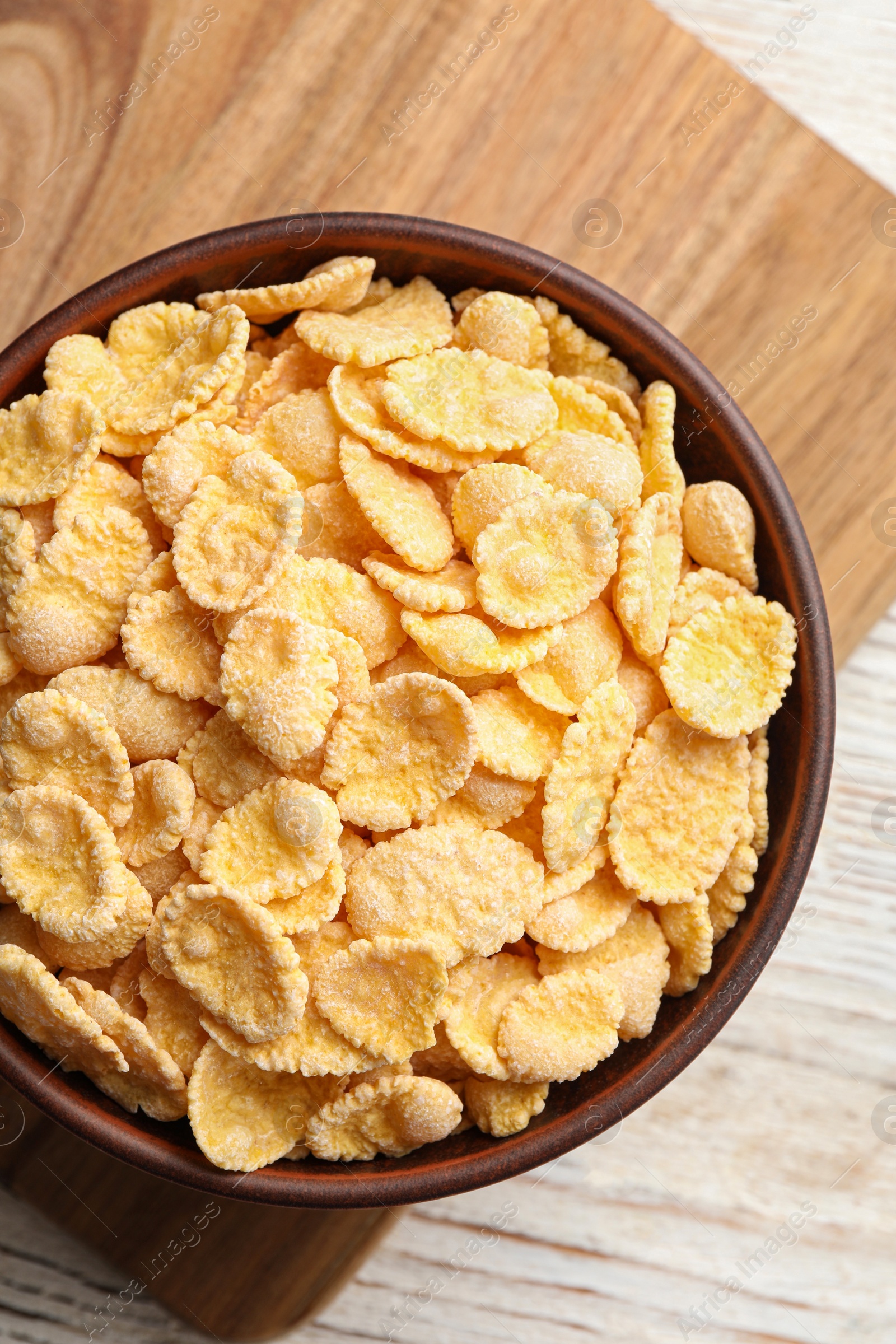 Photo of Bowl of tasty corn flakes on wooden table, top view