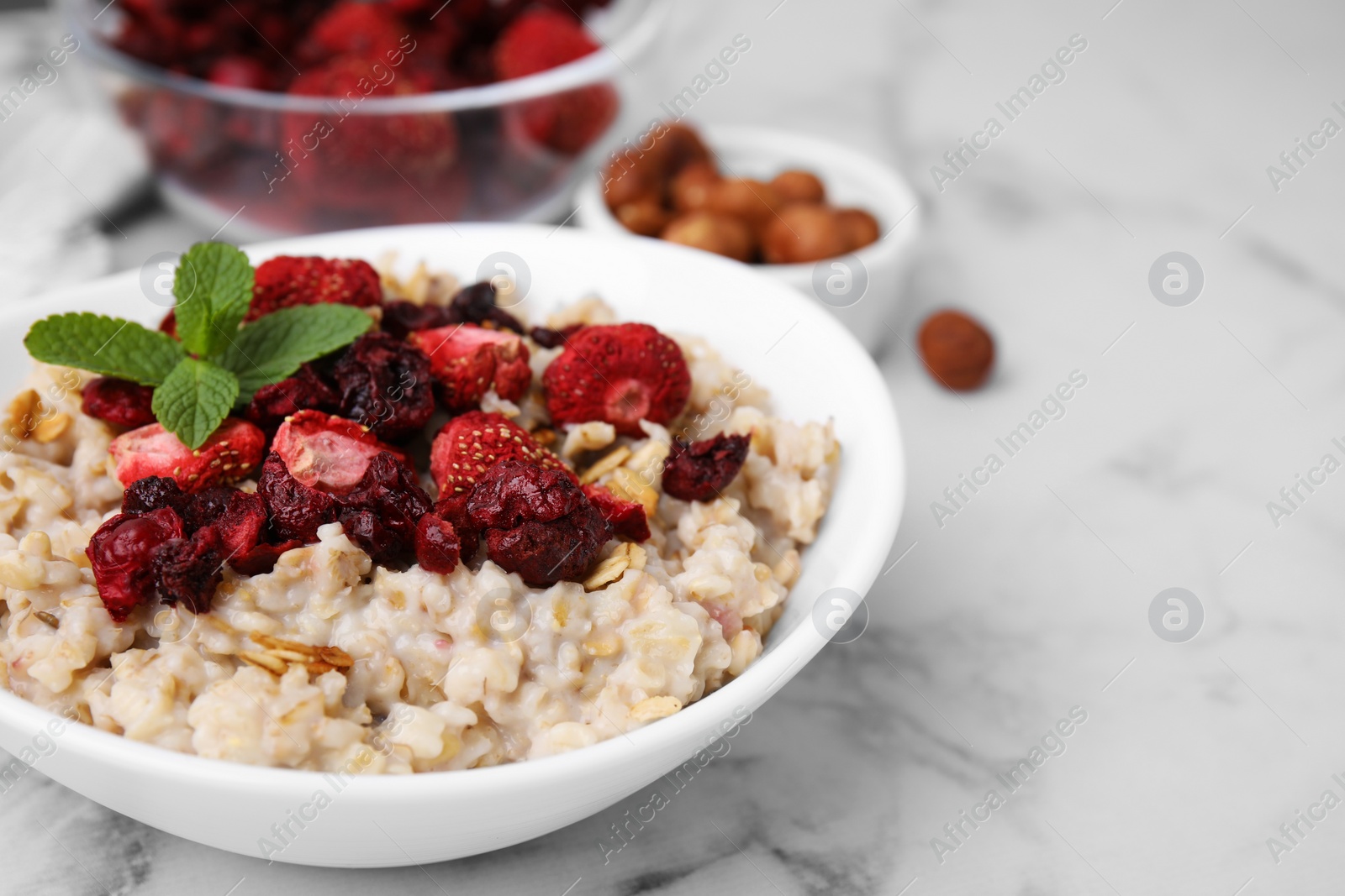 Photo of Oatmeal with freeze dried strawberries and mint on white marble table, closeup. Space for text