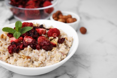 Photo of Oatmeal with freeze dried strawberries and mint on white marble table, closeup. Space for text