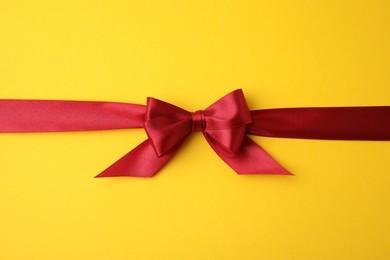 Photo of Red satin ribbon with bow on yellow background, top view