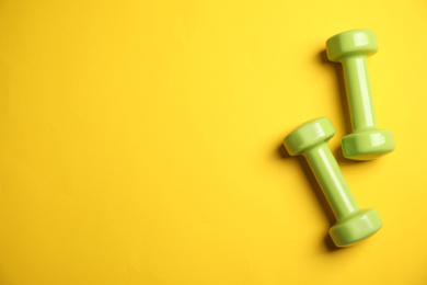 Photo of Top view of modern green dumbbells on yellow background, space for text. Physical fitness