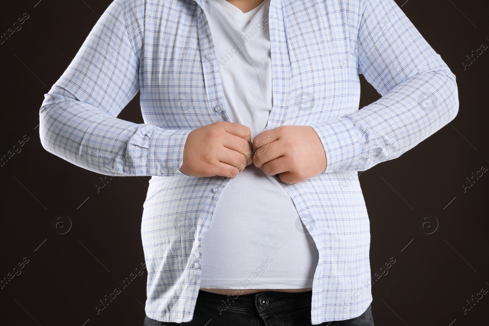 Photo of Overweight man trying to button up tight shirt on dark brown background, closeup