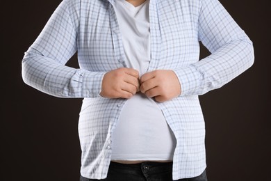 Overweight man trying to button up tight shirt on dark brown background, closeup