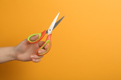 Photo of Woman holding office scissors on yellow background, closeup. Space for text