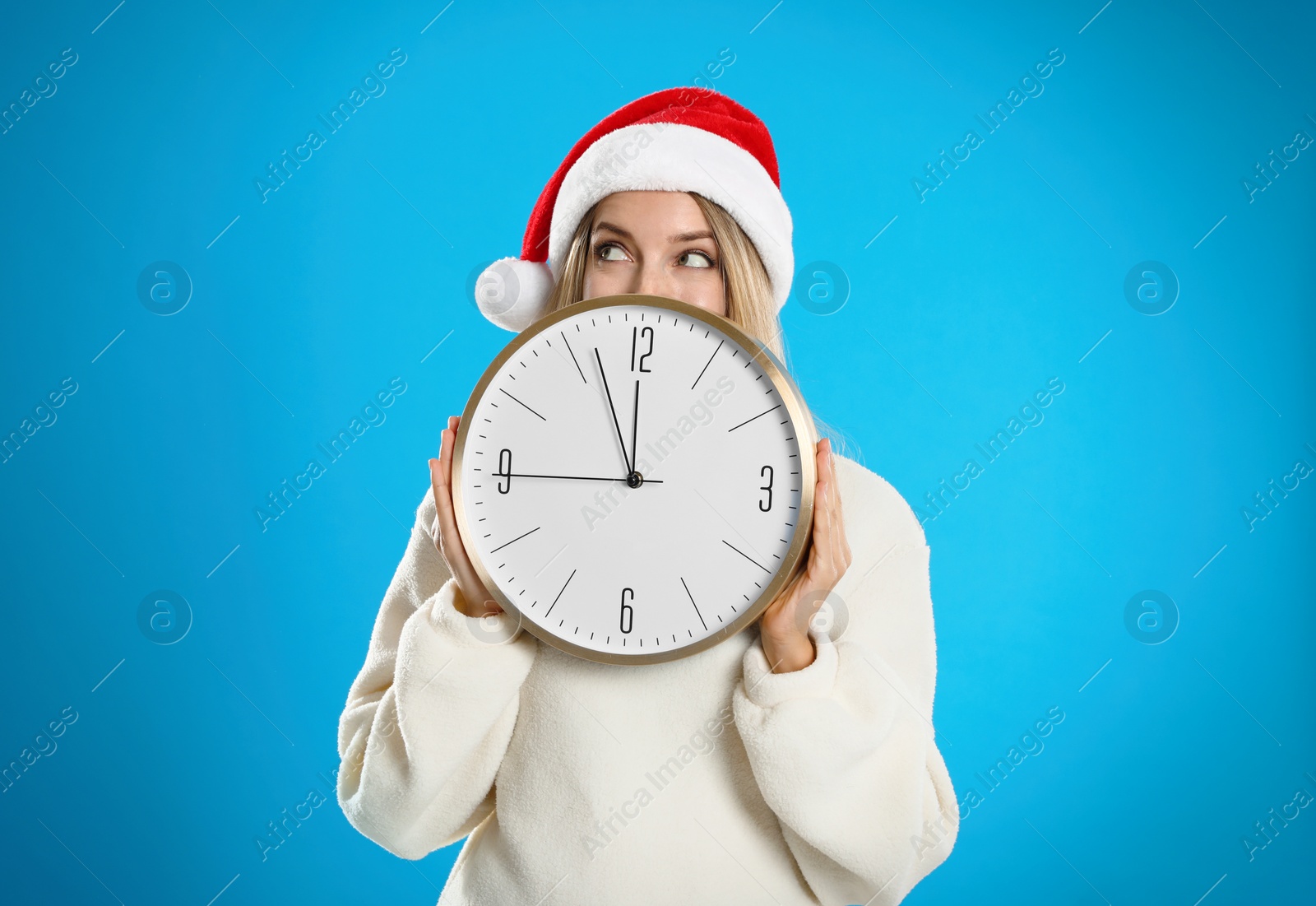 Photo of Woman in Santa hat with clock on light blue background. New Year countdown