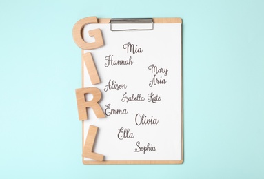 Photo of Clipboard with list of baby names and wooden letters on light blue background, top view