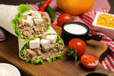 Delicious tortilla wraps with tuna and products on wooden board
