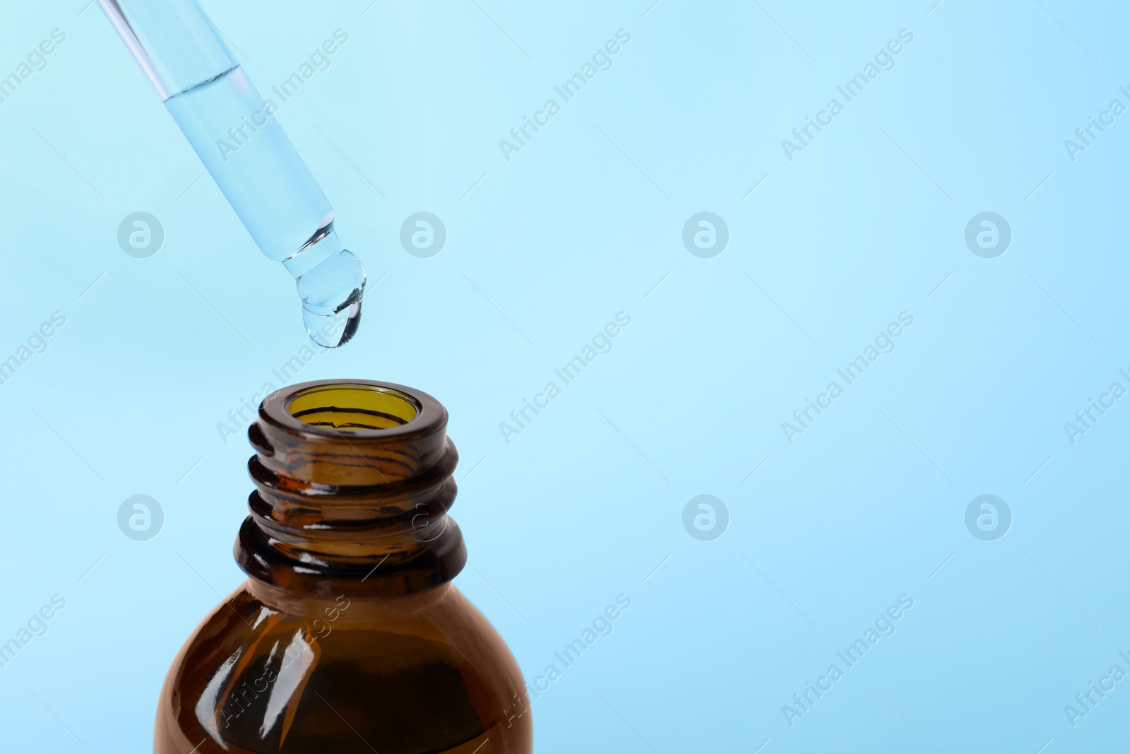 Photo of Dropping cosmetic oil from pipette into bottle on light blue background, closeup. Space for text