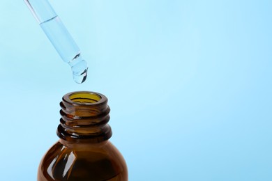 Photo of Dropping cosmetic oil from pipette into bottle on light blue background, closeup. Space for text