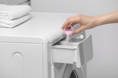 Photo of Woman pouring fabric softener from cap into washing machine on light grey background, closeup