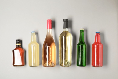 Bottles with different alcoholic drinks on light background, top view