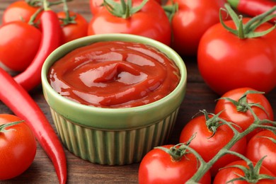 Photo of Bowl of tasty ketchup, chili peppers and tomatoes on wooden table, closeup