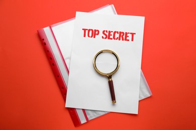 Top Secret stamp. Magnifying glass, sheet of paper and folder on red background, top view