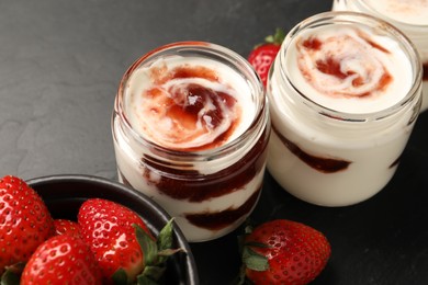 Photo of Tasty yoghurt with jam and strawberries on black table, closeup