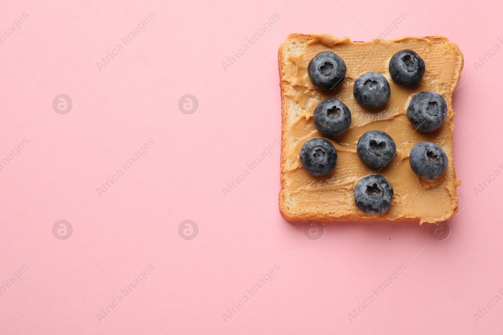 Photo of Tasty peanut butter sandwich with fresh blueberries on pink background, top view. Space for text