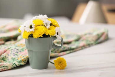 Beautiful bright flowers in cup and fabric on white marble table, space for text