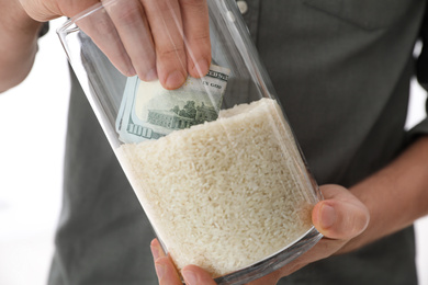 Photo of Man hiding money in jar of rice indoors, closeup. Financial savings