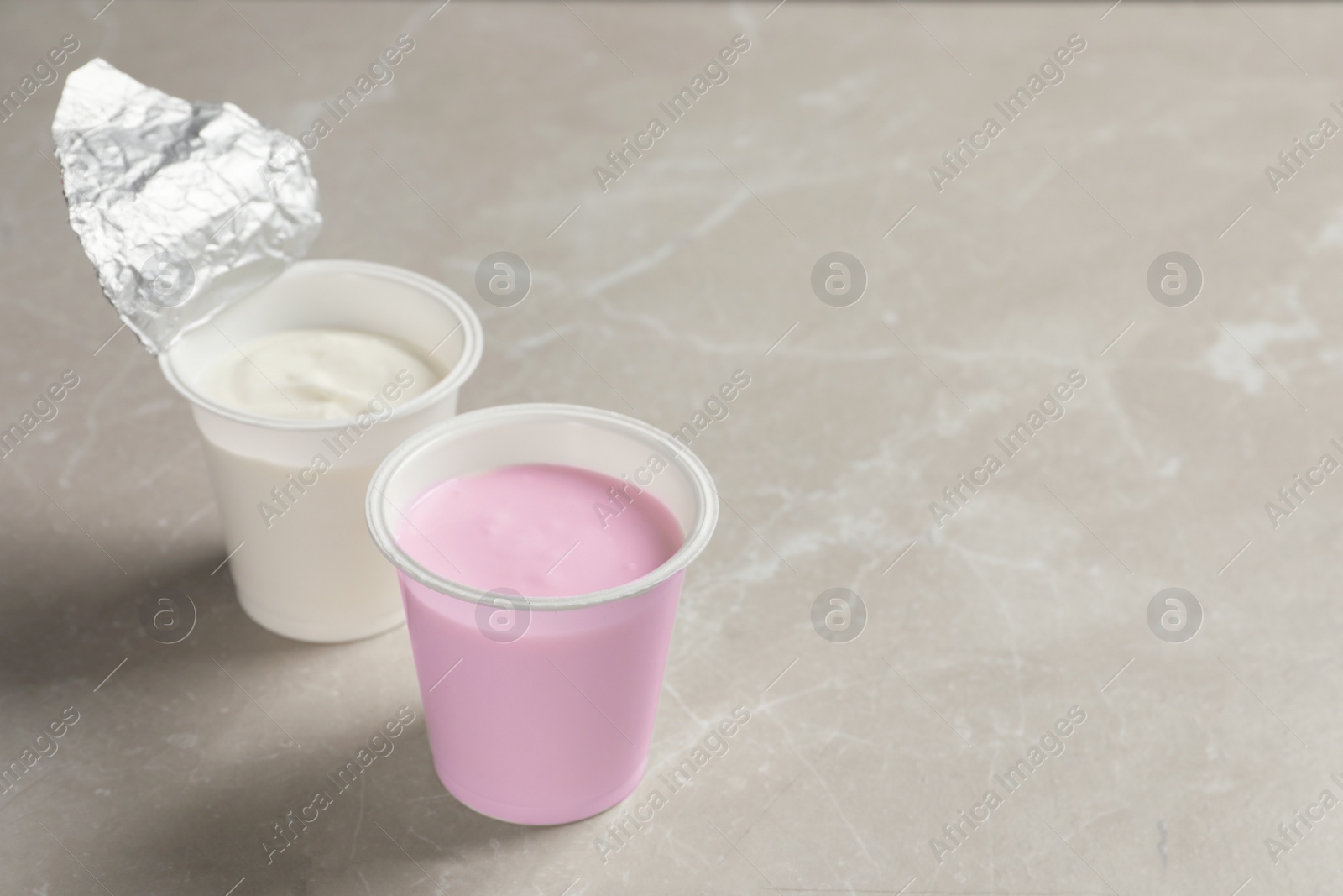 Photo of Plastic cups with delicious organic yogurt on grey marble table, space for text