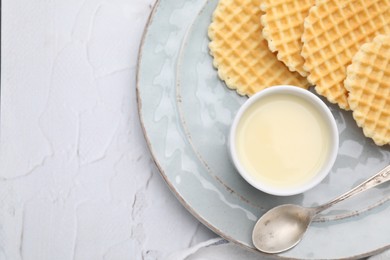 Photo of Tasty waffles served with condensed milk on white textured table, top view. Space for text