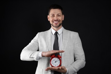 Photo of Happy businessman holding alarm clock on black background. Time management
