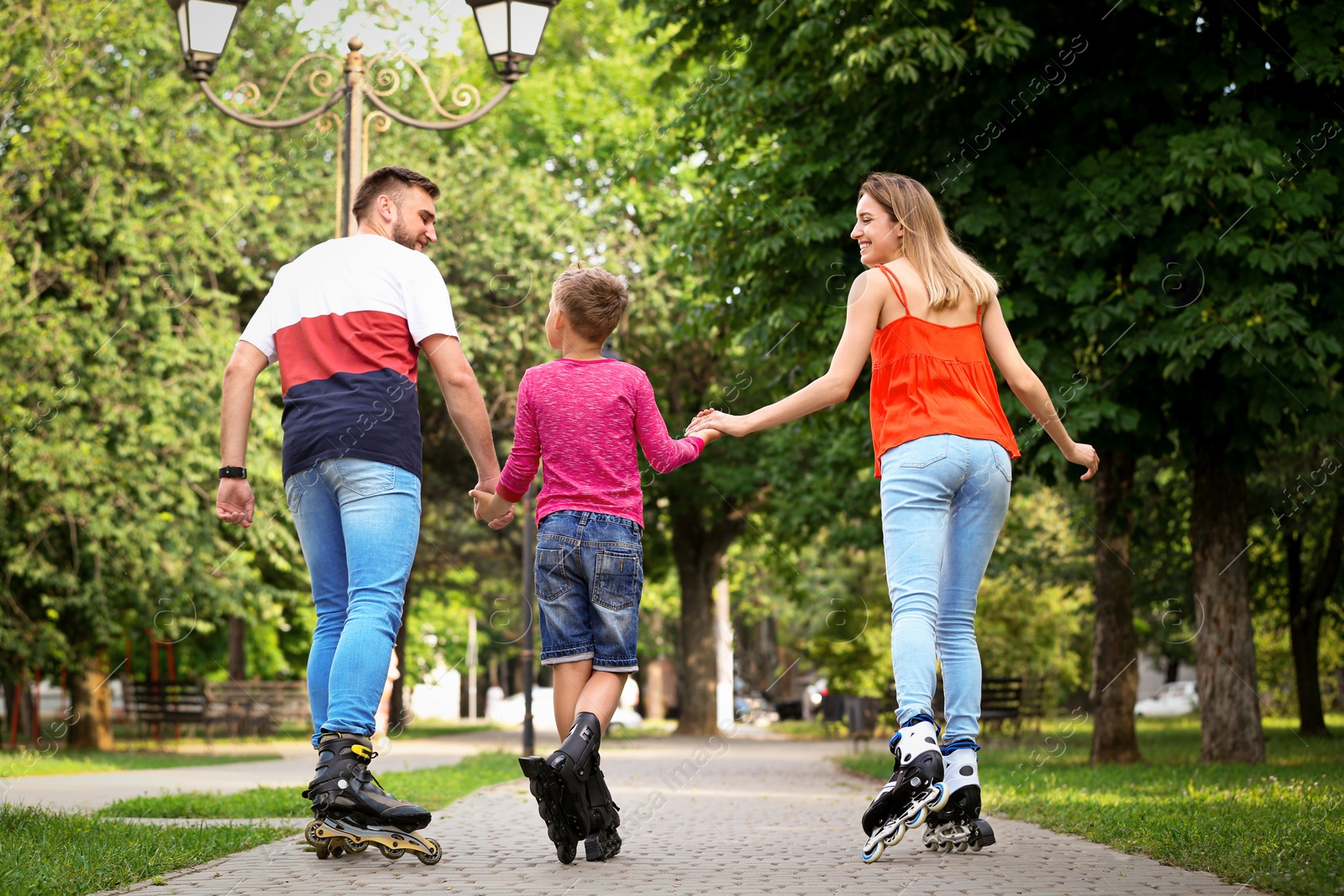 Photo of Young family roller skating in park, back view