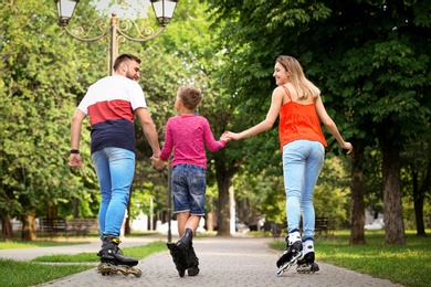 Photo of Young family roller skating in park, back view
