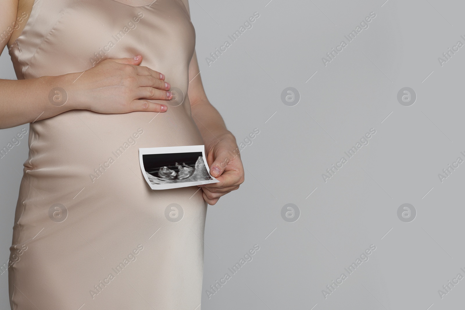 Photo of Pregnant woman with ultrasound picture of baby on light grey background, closeup. Space for text