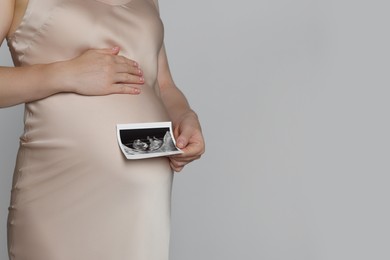 Photo of Pregnant woman with ultrasound picture of baby on light grey background, closeup. Space for text