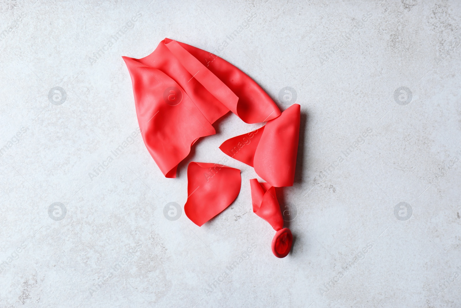 Photo of Popped red balloon on grey background, top view