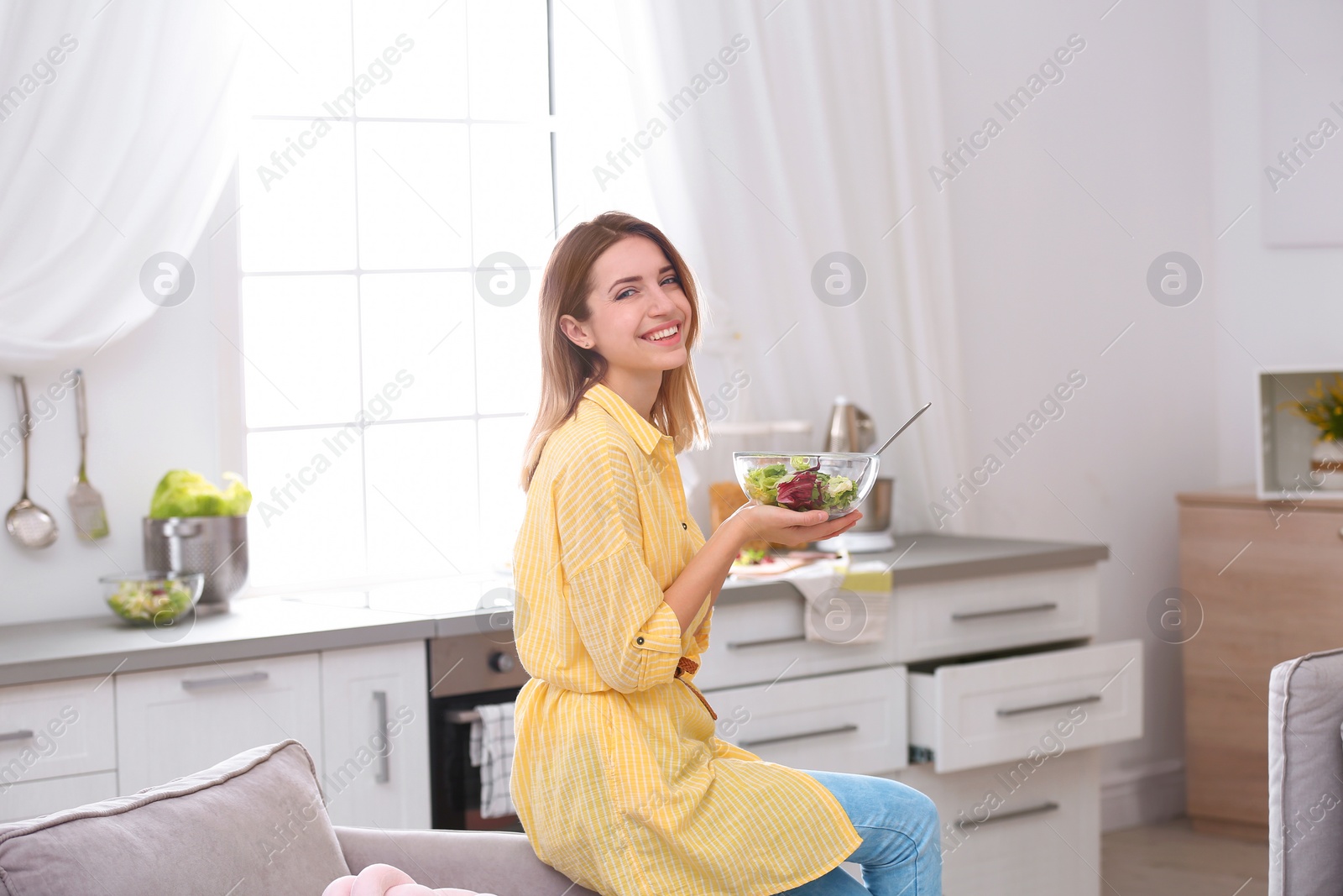 Photo of Happy young woman eating salad in kitchen. Healthy diet