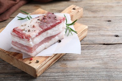 Photo of Tasty salt pork with rosemary and spices on wooden table, space for text