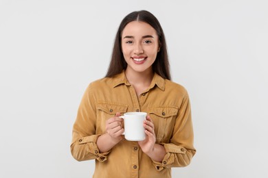 Photo of Happy young woman holding white ceramic mug on light grey background
