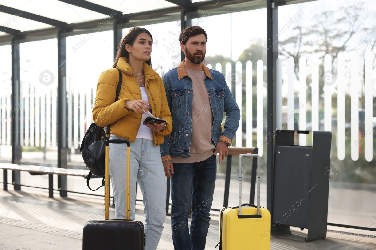 Photo of Being late. Worried couple with suitcases waiting at tram station outdoors