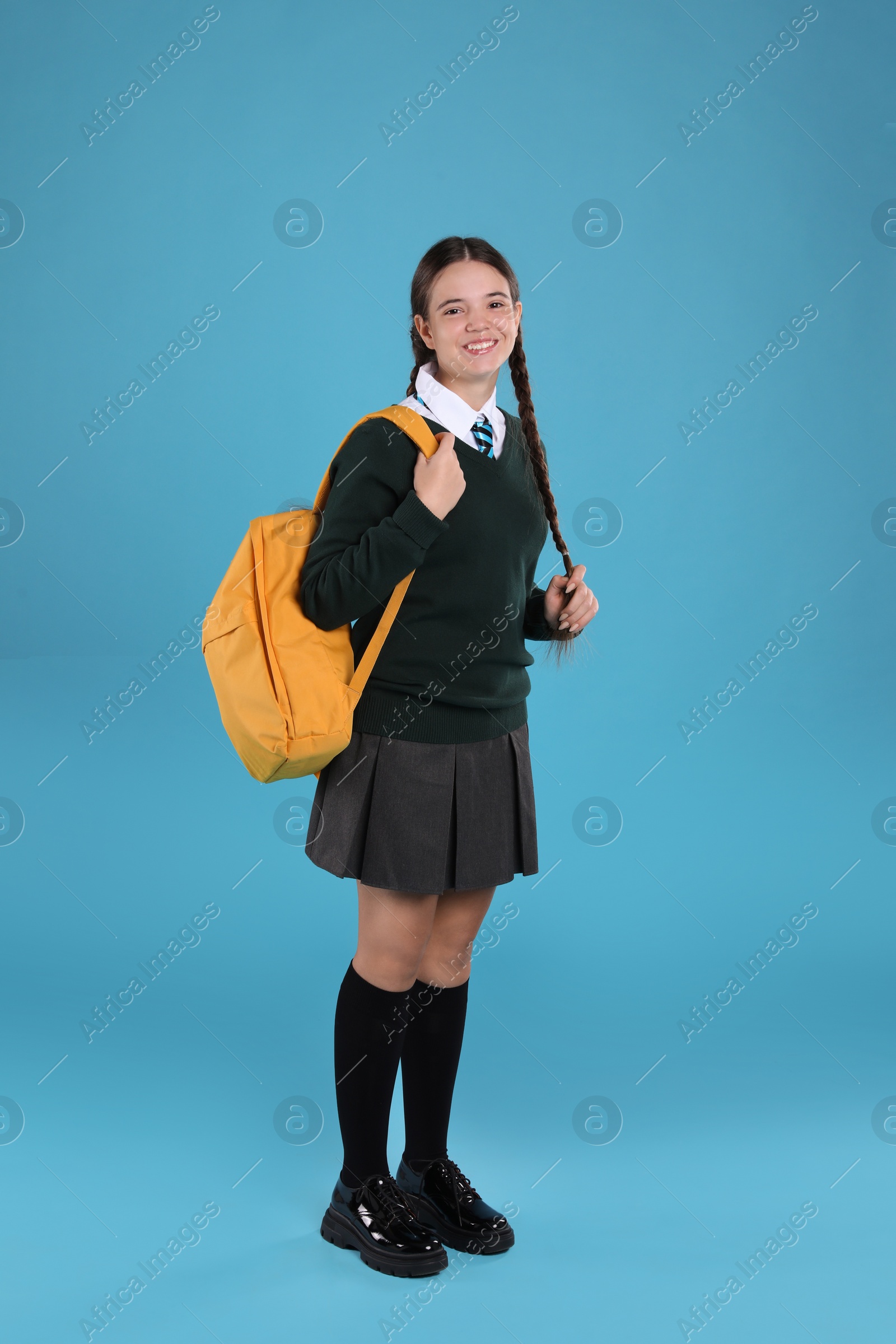 Photo of Teenage girl in school uniform with backpack on light blue background