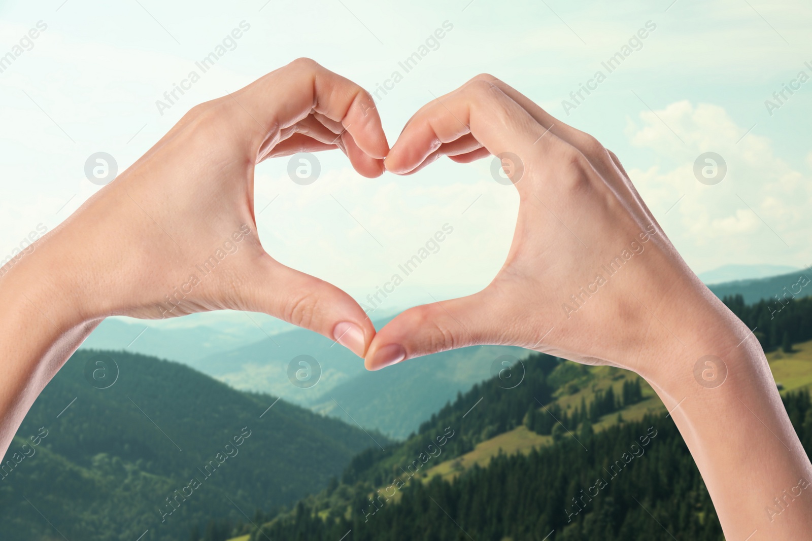 Image of Woman making heart with hands in mountains on sunny day, closeup