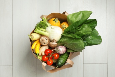 Photo of Paper bag full of fresh vegetables on light background, top view