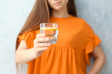 Young woman holding glass of lemon water on color background, closeup