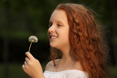 Happy girl with red hair holding dandelion in park