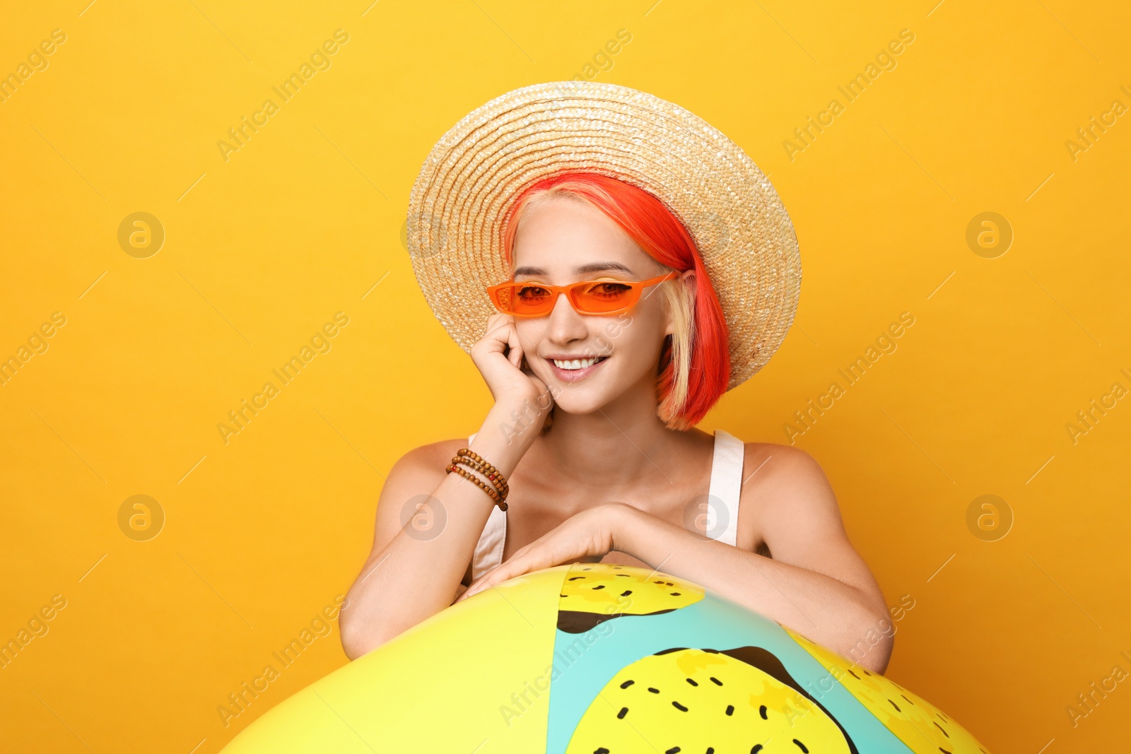 Photo of Beautiful young woman with bright dyed hair and inflatable ball on orange background